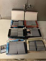 Overhead view showing six boxes filled with Magic: The Gathering cards in sleeves and stacks within various card boxes.