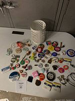Collection of assorted pins displayed alongside a white plastic lattice candle holder on a white table.