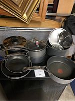 Various pots, pans, and lids grouped together on a flat surface showing assortment of cookware