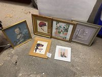 Full view of six framed artworks and decor items arranged on a floor, showing variety in style and frames.