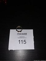 Full view of the metal ring laying on a numbered card, showing its circular shape and three rounded details.