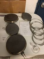 Photo showing 4 smart burner elements, 4 metal mounting rings, instruction manual and roll of tape on table.