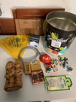 Full view of lot including Smurf figurines, mushroom figurine, wooden statue, picture frames, wire, cigarette packs, and popcorn tin