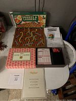 Photo showing the wooden Snakes & Ladders board game laid open beside the boxed Five of a Kind game and instruction manuals.