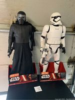 Two Star Wars figurines Kylo Ren and Stormtrooper standing side by side in original packaging bases.