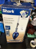 Box of Shark Deluxe steam mop with blue and gray mop body shown on front and usage information.
