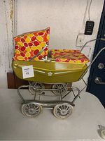 Side view of vintage green doll stroller with colorful yellow, orange, red canopy and white flower decal on body