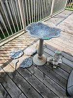 Full view of bird bath with scalloped edge and pedestal base alongside garden ornaments and plastic girl figurine on bench.