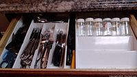 Drawer organizer with assorted flatware - forks, knives including ornate Oneda flatware, black handled knives, scissors, and plastic spice bottle rack.