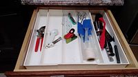 Drawer with kitchen utensils including can opener, measuring spoons, spatulas, silicone brush, thermometer, scissors, knives