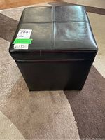 Front view of black leather foot stool showing square shape and stitched cushion top.