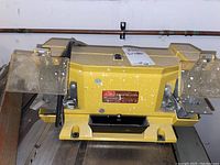 Front view of yellow Shopmate 6 inch bench grinder with motor compartment, dual grinding wheels, and clear safety shields on each side. Power cord visible.