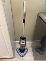 Full view of Hoover steam mop upright on tiled floor with triangular mop head and microfiber pad.