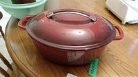 Front side view of the red enamelled cast iron Dutch oven with lid on wooden table.