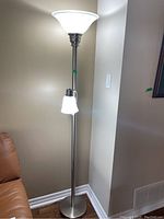 Full view of the floor lamp turned on, showing the large frosted glass shade at the top and smaller secondary light below on a flexible arm, standing next to sofa.