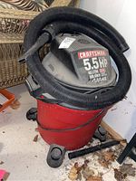 Front view of Craftsman shop vacuum showing red base tank with four caster wheels, black top motor housing, and coiled black hose.