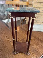 Full view of the wood pedestal table showing green stone top, wood legs with gold rings, and decorative accents at corners.
