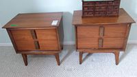 Two wooden side tables with two drawers each, standing on carpeted floor, viewed from front.