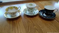 Three different teacup and saucer pairs on wooden surface, showing designs and colors.
