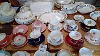 Eight assorted bone china teacups and saucers arranged on table with background serving pieces