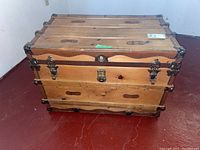 Full view of rectangular wooden trunk on floor showing the top, front, and side with metal hardware.