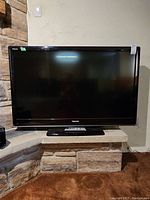 Front view of the Toshiba 52 inch television placed on a stone ledge with remote on base stand.