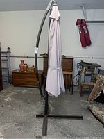 Full view of closed beige patio umbrella on dark brown curved metal stand with cross base