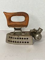 Side view of vintage Joseph Feldmeyer flat iron displaying wooden handle and metal body with ventilation holes, methylated spirit fuel chamber attached.