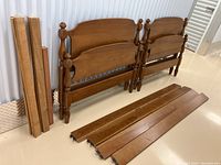 Two maple twin headboards and footboards leaning against wall with side rails and slats laid out in front