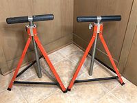 Photo showing two adjustable saw rollers side by side against corner walls on a tiled floor.