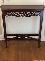 Full view of dark-finished wooden hall table showing carved scroll and shell motifs on front apron, straight legs, and decorative stretcher.