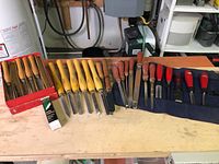 Wide view showing assortment of chisels with wooden and red handles, boxed and rolled for storage.