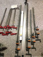 Full view of assorted large bar clamps in various sizes and the Tru-Grip Clamp 'N Tool Guide tool lined up on the floor.