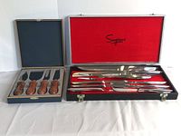 Photo showing Simpsons branded cutting tool set with multiple knives and forks in a red-lined case, and Gowlings cheese serving set with four wooden handled cheese knives in a grey-lined box.