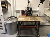 Front view of Eaton Viking radial arm saw on metal stand with wooden table, dust collector bin to left.