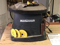 Front view of black Mastercraft oscillating spindle sander with yellow sanding discs placed in front