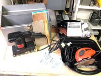 Craftsman Ideal Motion Sander with sandpaper sheets beside it and part of the Black & Decker box visible
