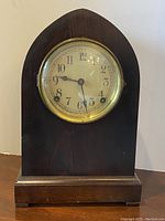 Full front view of the wooden mantel clock showing the arched top and clock face.