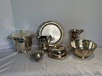 Group photo of all seven silver plated serving items together on white cloth background showing reflective surfaces and variety of item types