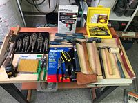 Full layout of assorted hand tools including locking pliers, glue gun in box, yellow tool box with metal tools, screwdrivers, hammers, tape measure, and packaged utility shears.