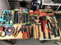 Full view of assorted hand tools laid on table showing pliers, hammers, wrenches, screwdrivers, snips, tape measures.