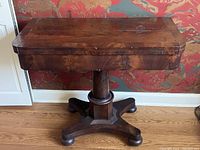 Front view of vintage wooden games table with closed top showing dark wood finish and pedestal base with cross-shaped feet.