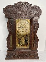 Front view showing detailed carved wooden case, clock face with brass bezel, thermometer on left, and barometer on right.