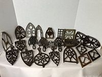Group display of assortment of 18 cast iron trivets in front of white backdrop