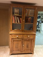 Full front view of assembled cabinet showing upper glass doors, lower drawers and doors with books inside.