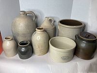 Photo of all eight vintage pottery pieces in the lot showing various sizes, cream, beige, and brown stoneware items including jugs, pots, and covered crocks.
