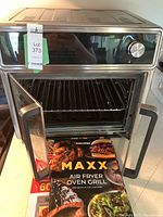 Open view of the Kalorik MAXX air fryer oven grill showing inside racks and recipe book at the front