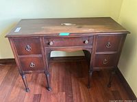 Front view of the antique wooden vanity desk showing five drawers, turned legs, and surface scratches.