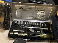 Stanley 40-piece ratchet and socket set including ratchet wrench, sockets, screwdriver handle, and extension bars in a metal toolbox with wear and rust on some items.