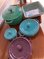 Five piece ceramic cookware set shown with various sized covered pots in green, purple, turquoise blue shades and one rectangular baking dish.